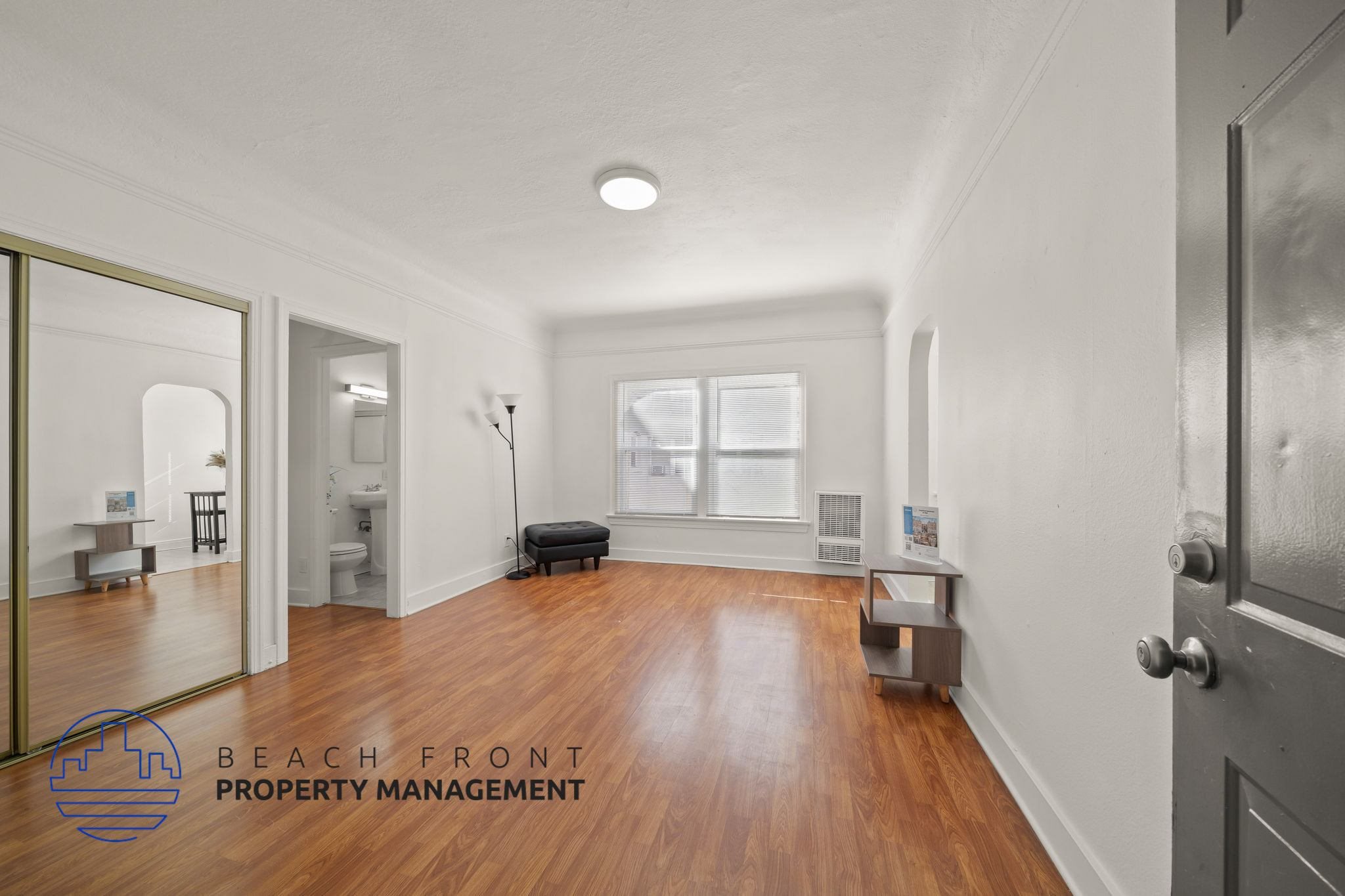 A spacious room with wooden floors and a large mirror on the wall.