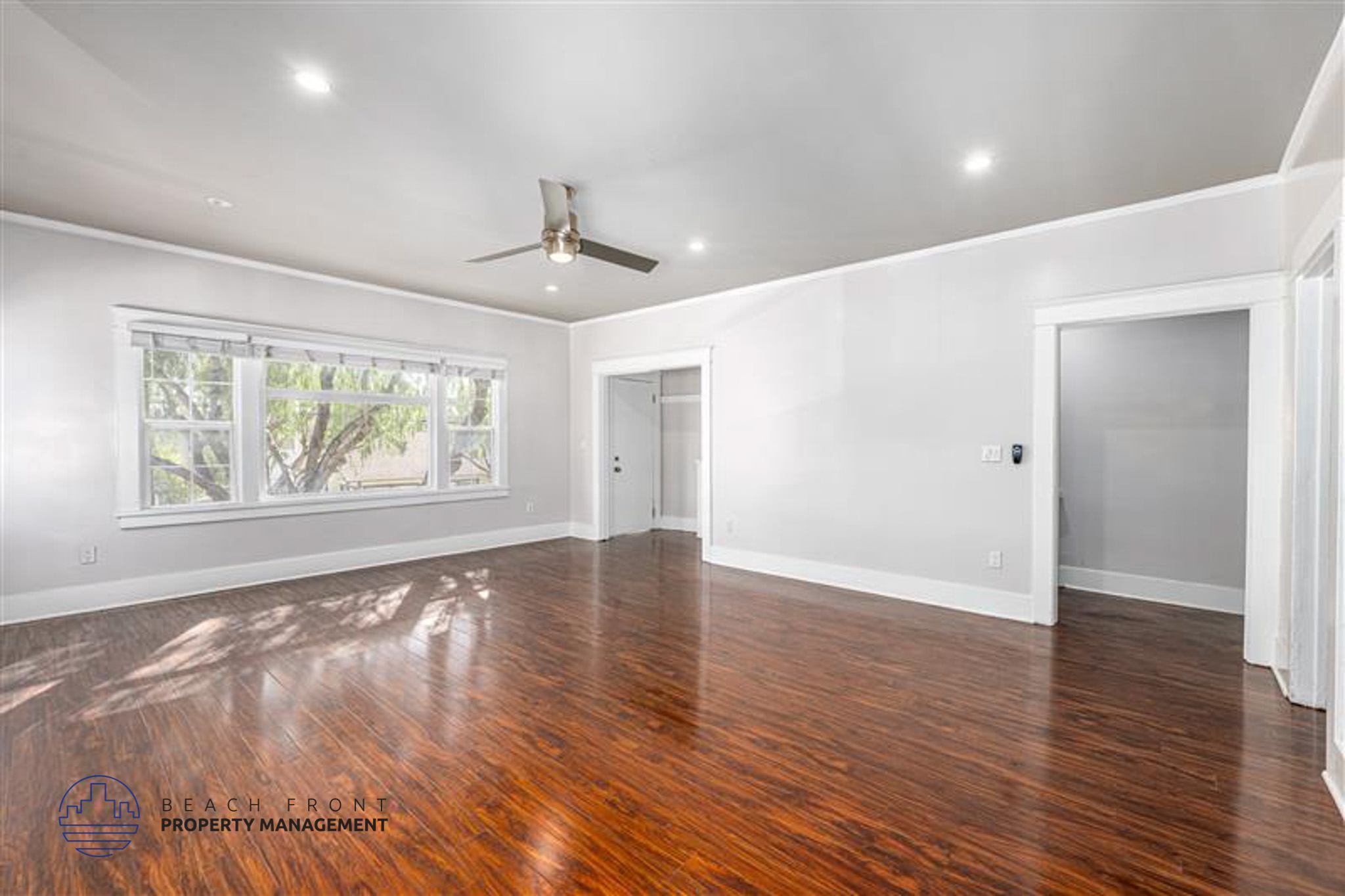 A spacious room with wooden floors and a ceiling fan.