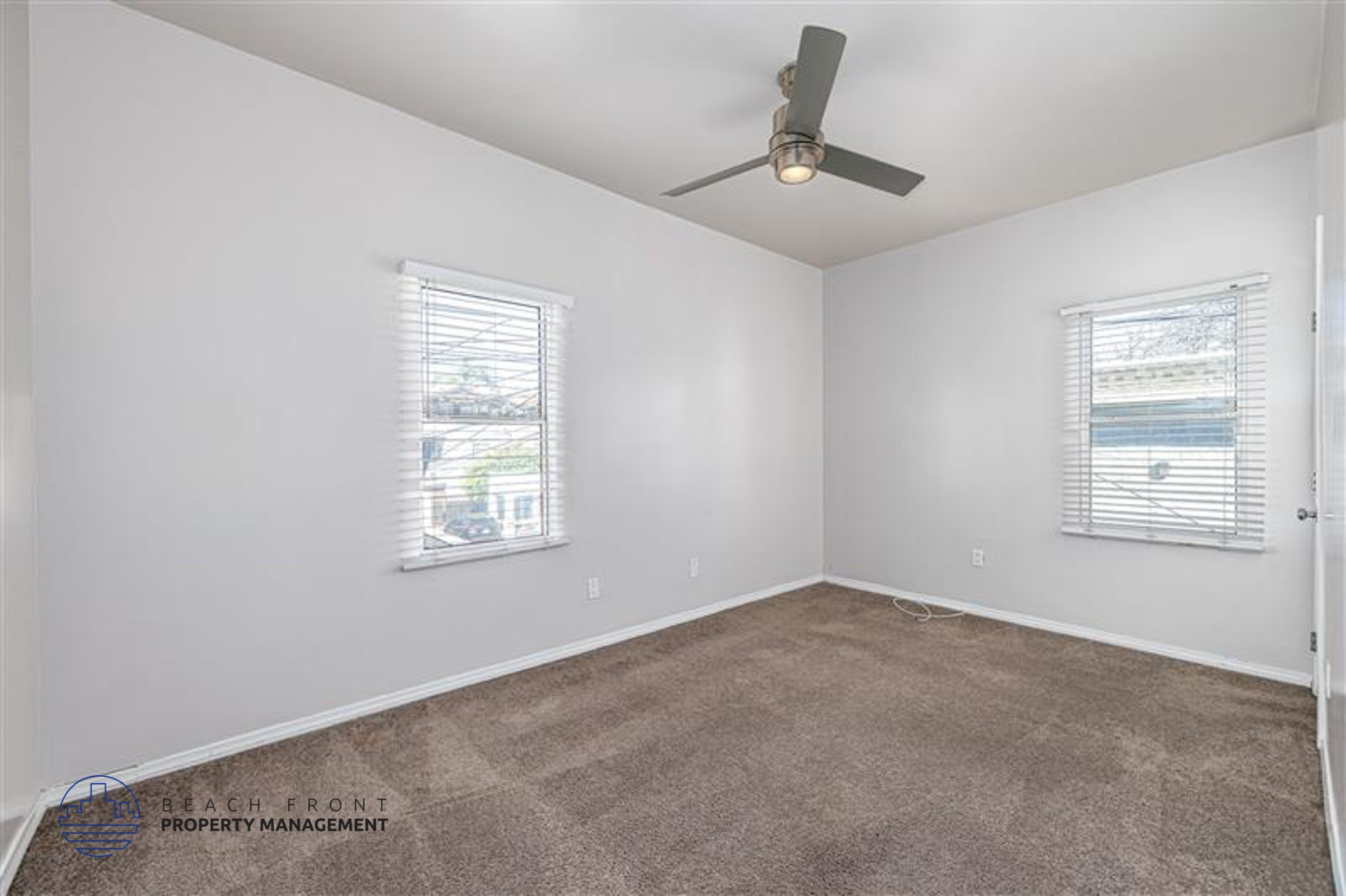 A room with a ceiling fan and two windows.