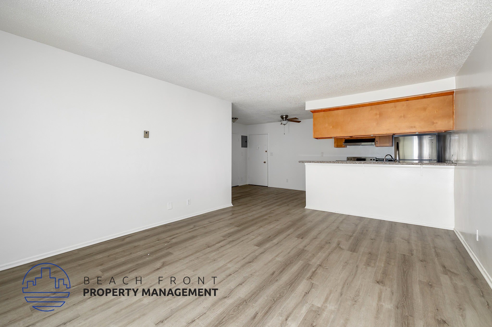 A room with wooden flooring and a white ceiling with a logo for Beach Front Property Management.