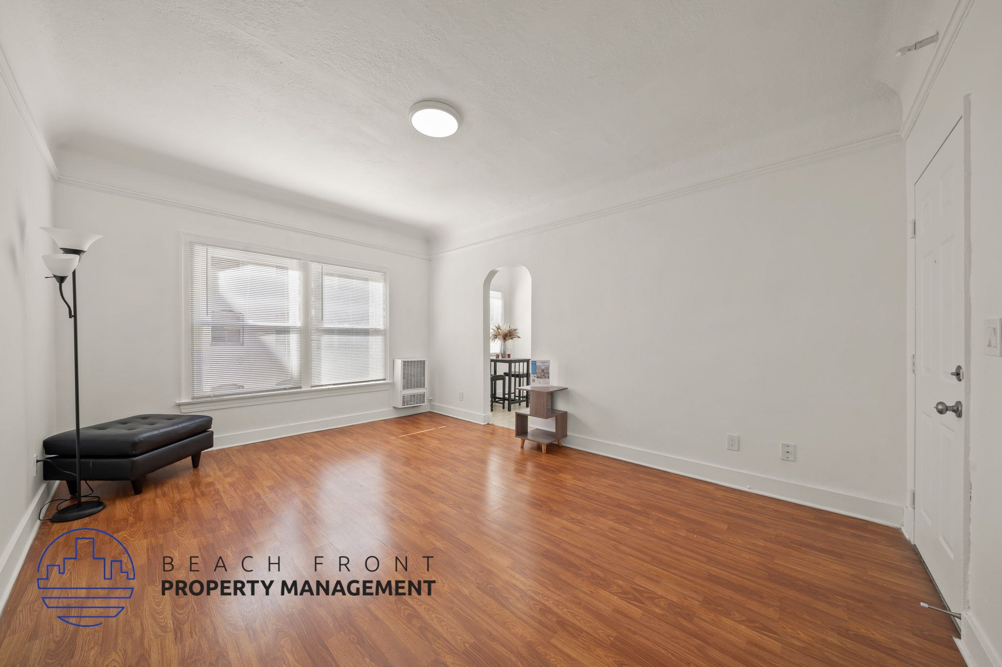 A room with wooden floors and white walls, with a logo for Beach Front Property Management in the bottom left corner.