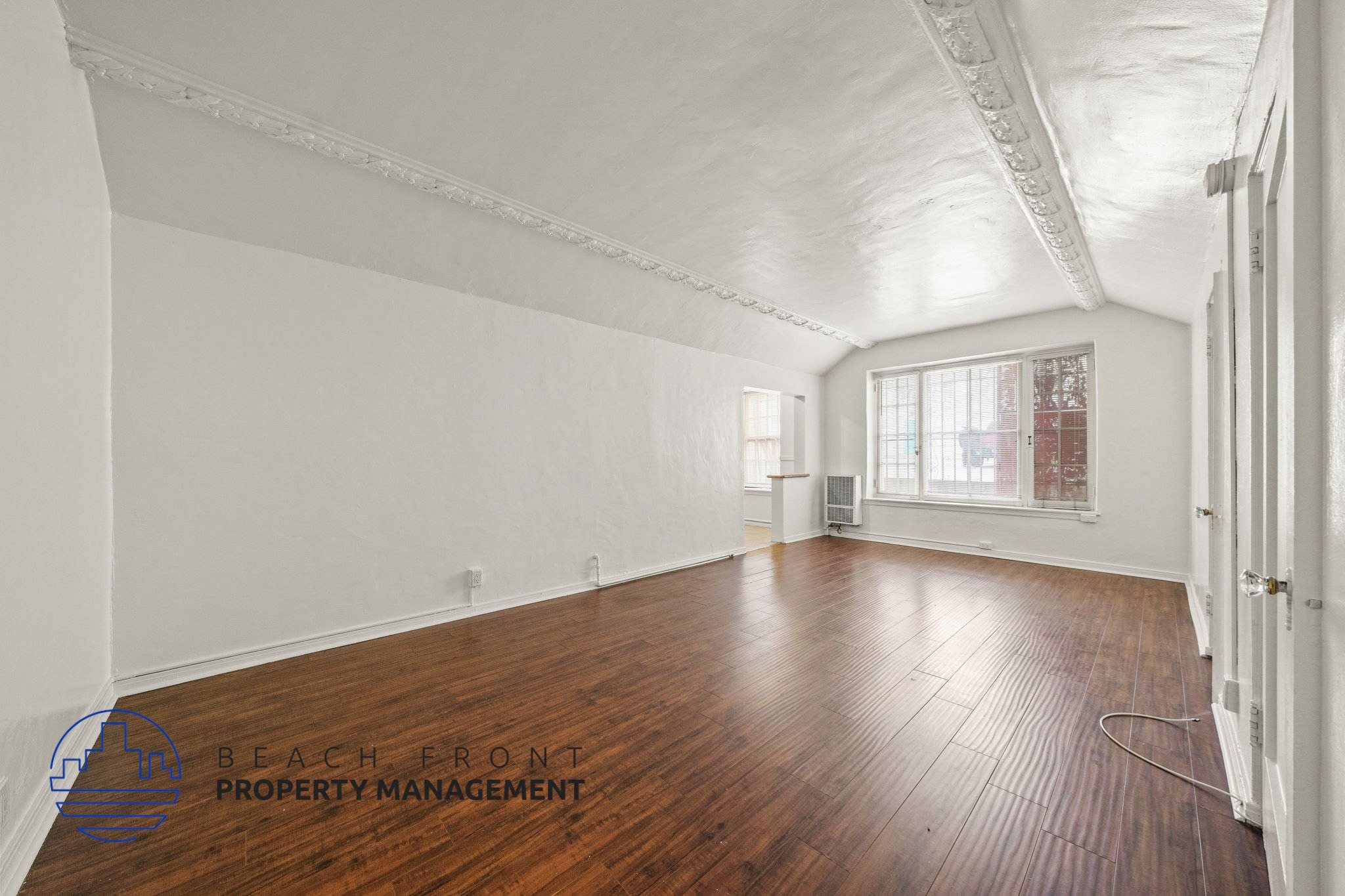 A room with wooden floors and white walls, with a window and a door visible.