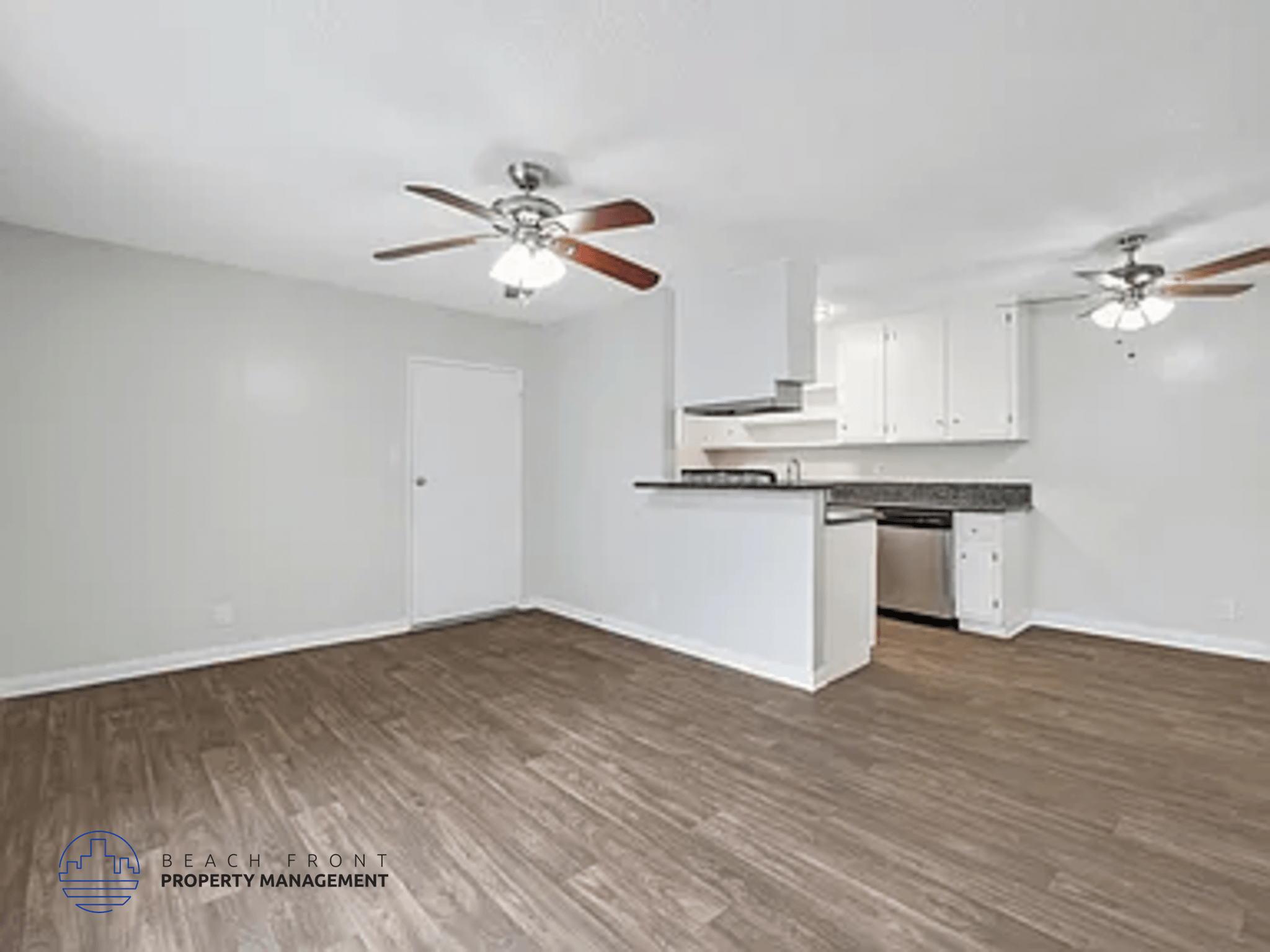 A spacious room with a kitchenette and two ceiling fans.