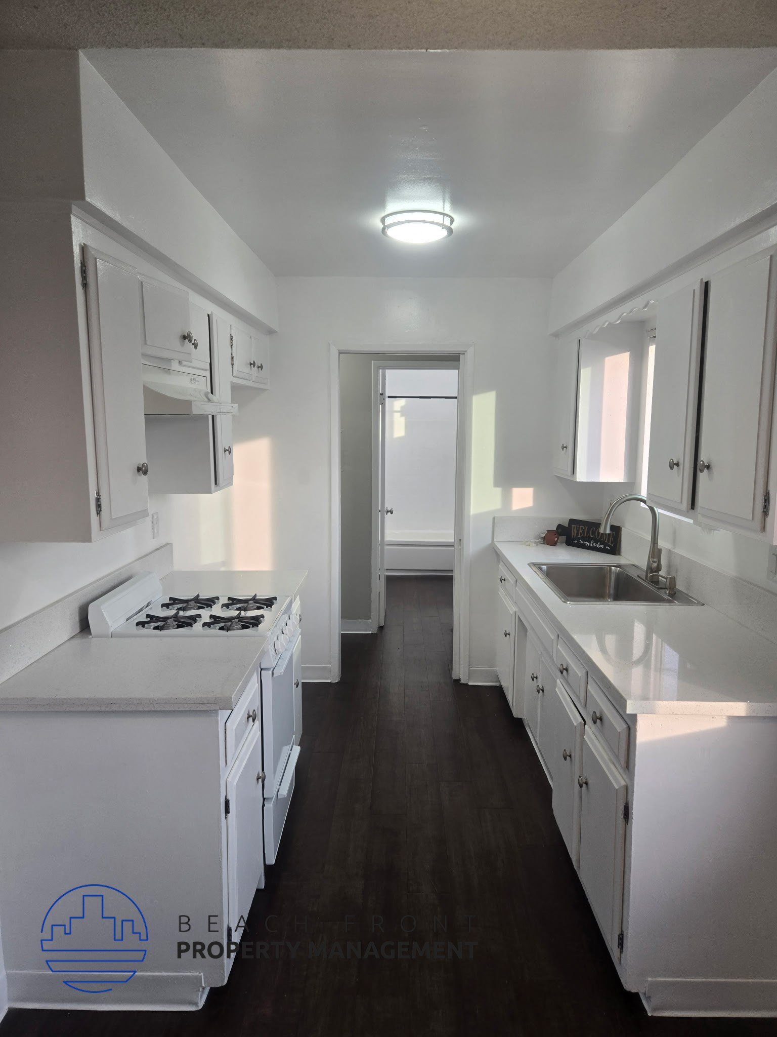 A clean, white kitchen with dark wood floors and a logo for Bel-Air Property Management in the bottom left corner.