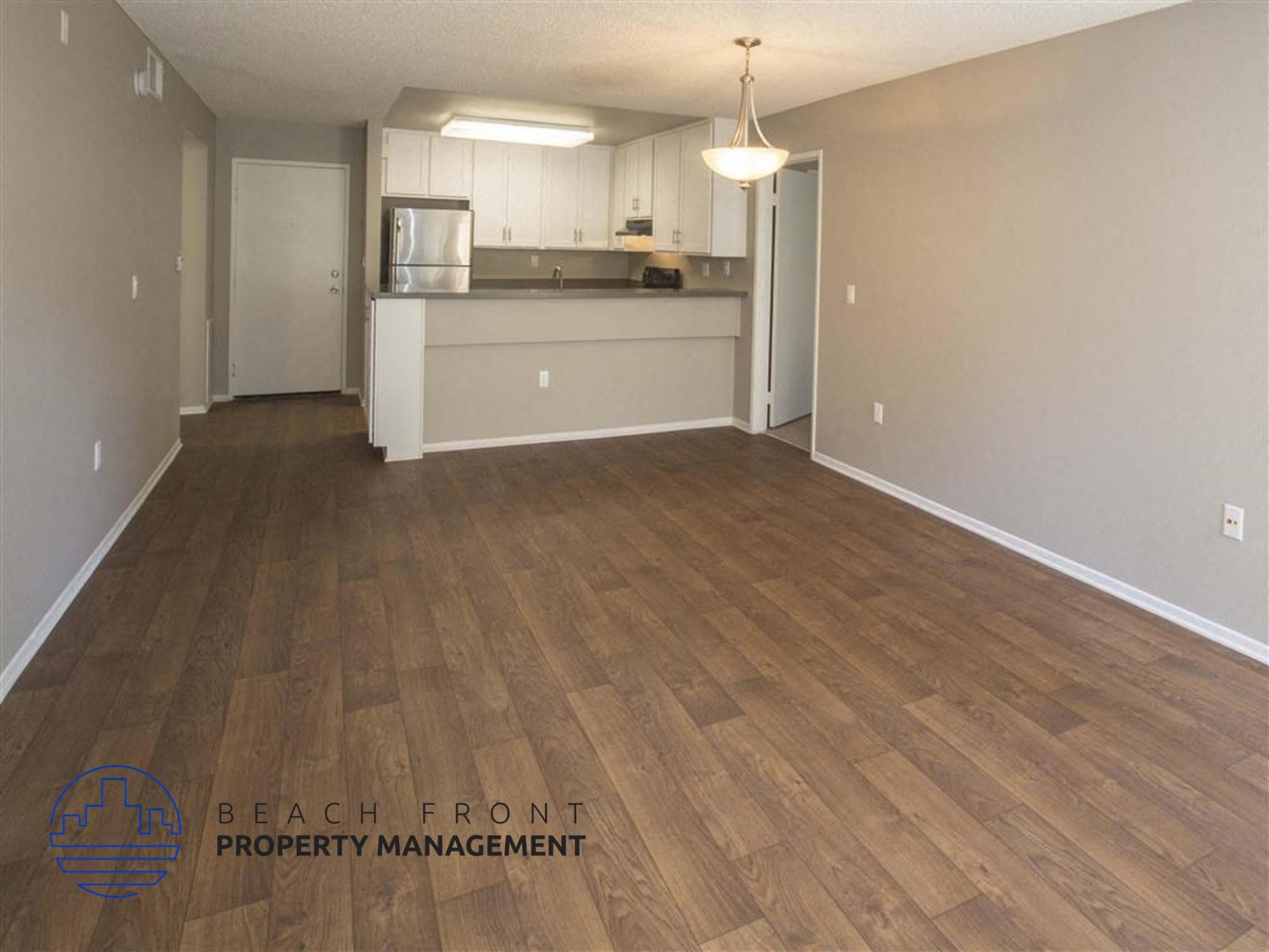 A spacious room with wooden flooring and a kitchen area in the background.