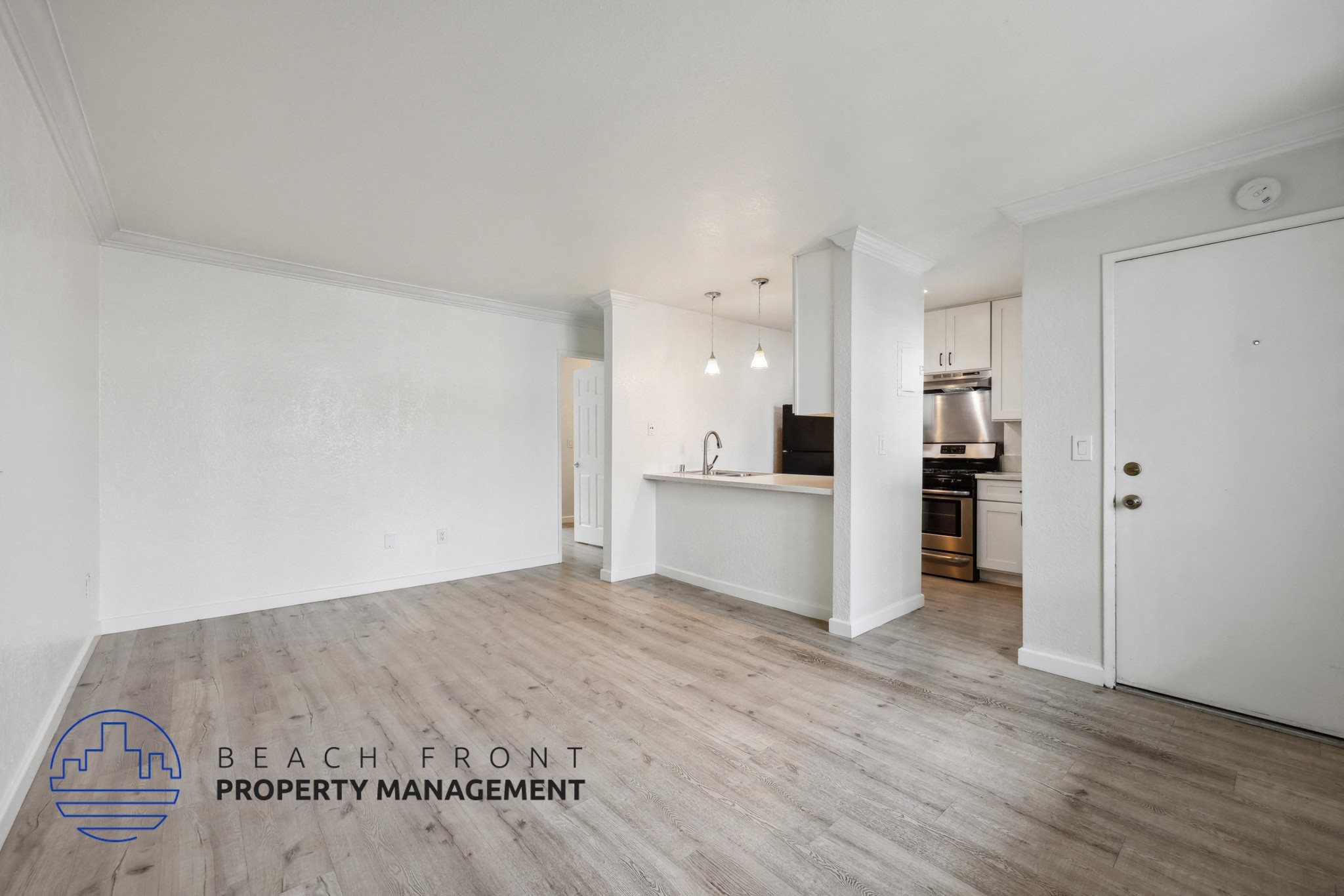 A spacious room with wooden flooring and a kitchen area in the background.