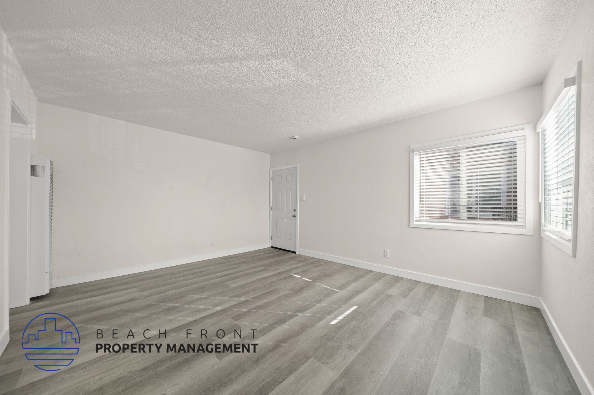 A room with a wooden floor and a window with blinds.