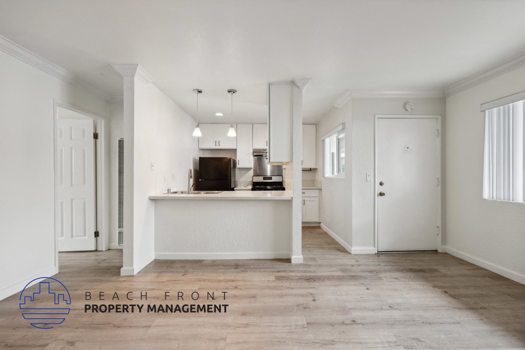 A spacious, empty room with a kitchenette and a logo for Beach Front Property Management.