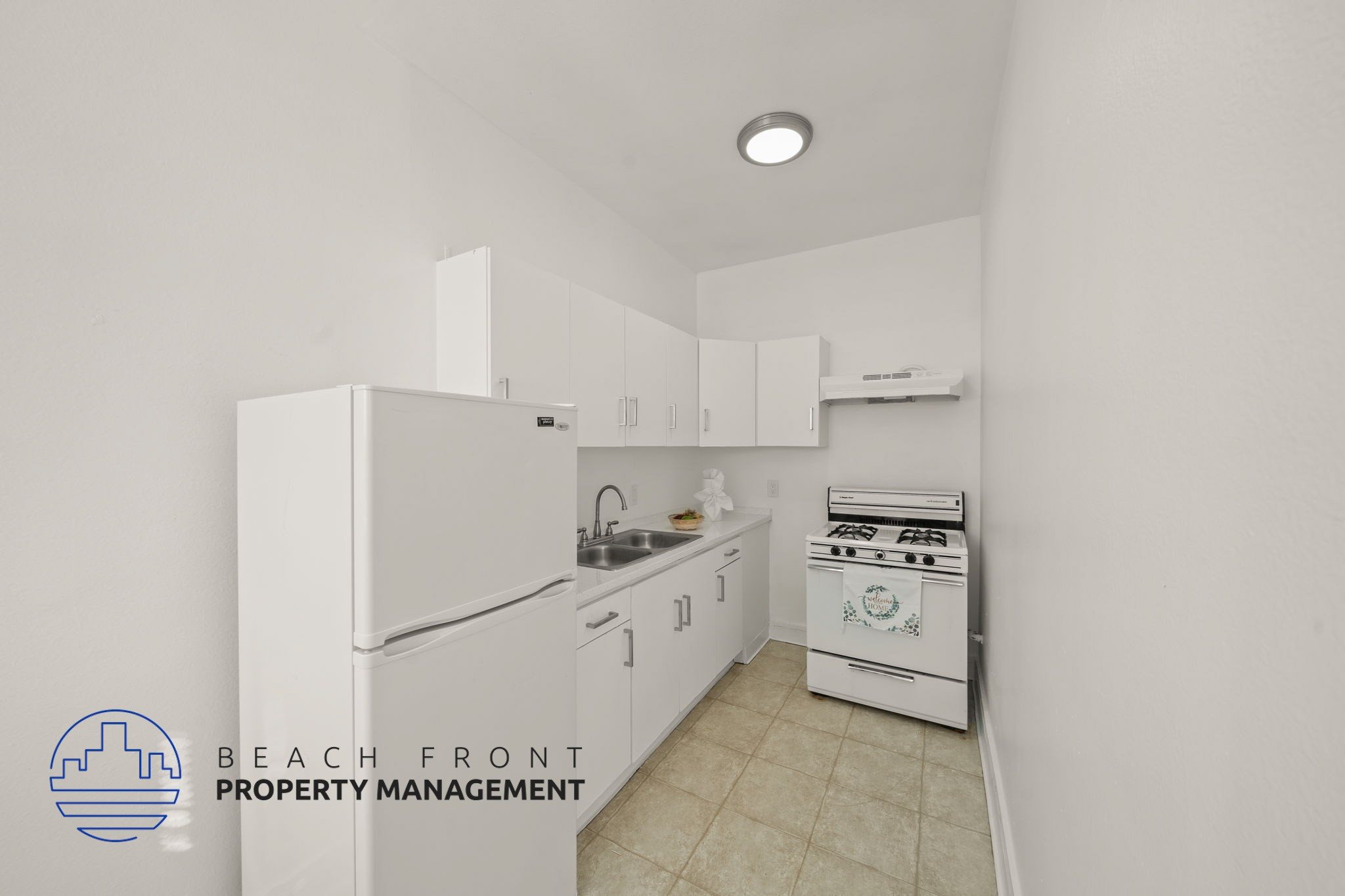 A kitchen with white appliances and cabinets, with a logo for Beach Front Property Management in the bottom left corner.