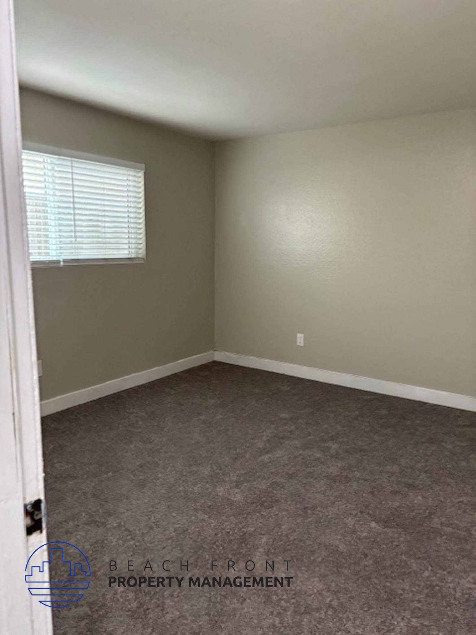 A room with a carpeted floor and a window with blinds.