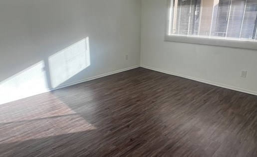 A room with wooden flooring and a window letting in sunlight.