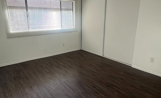 A room with wooden flooring and a window with blinds.
