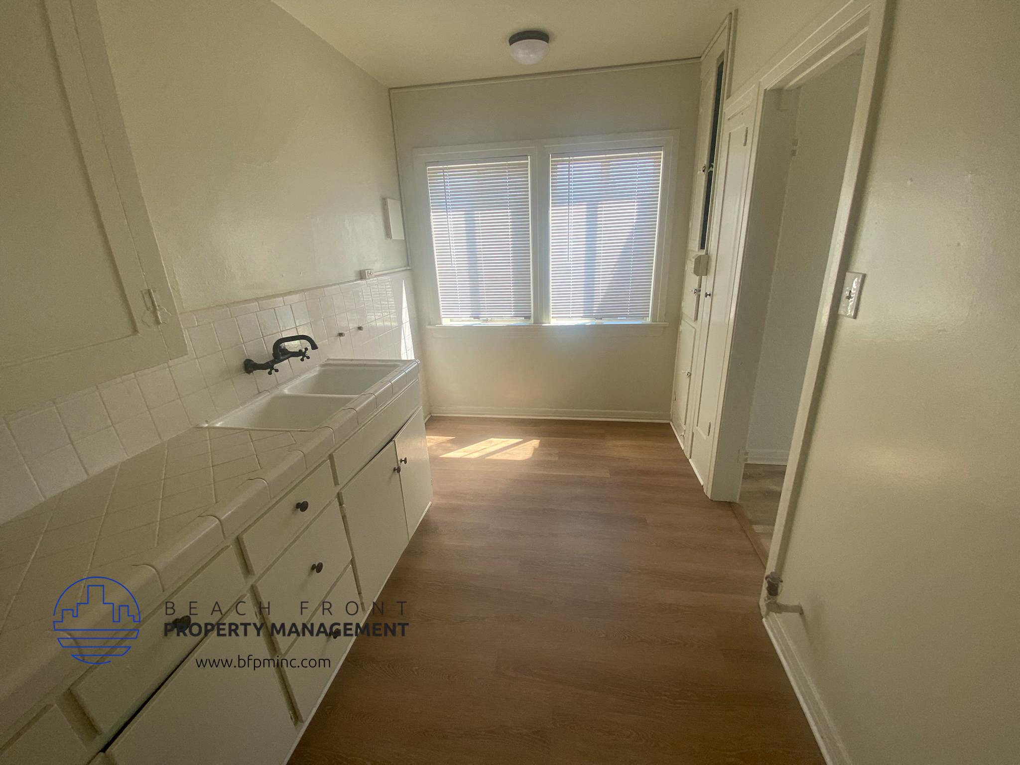 A white bathroom with a sink, mirror, and wooden floor.
