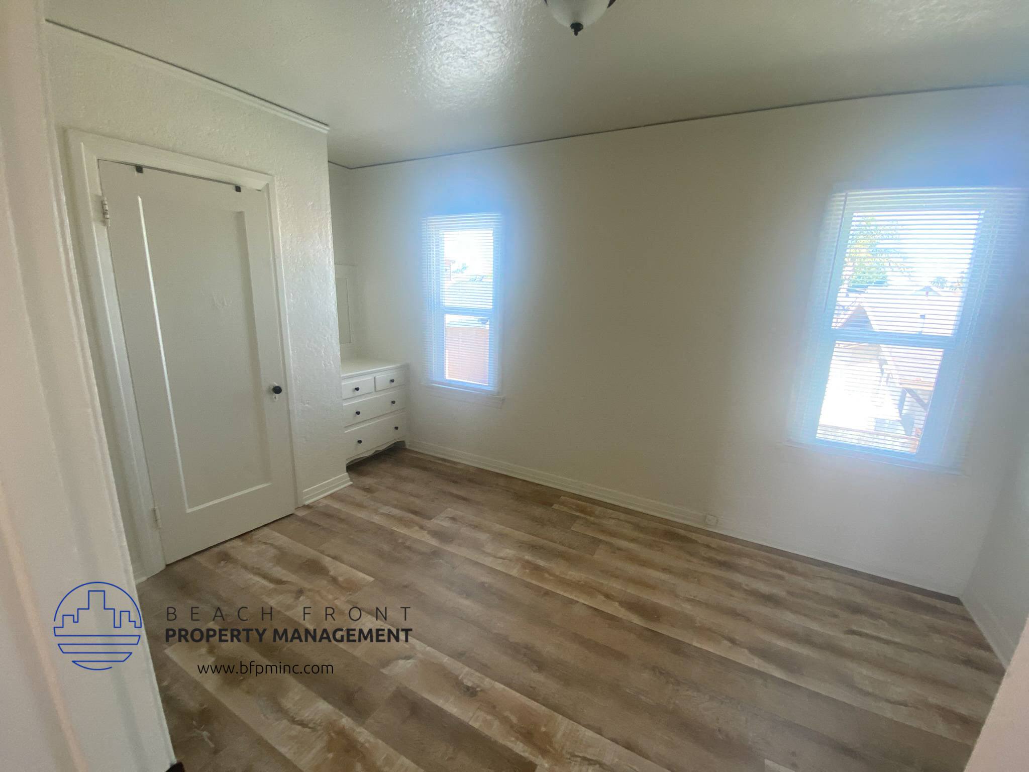 A room with wooden flooring and two windows.
