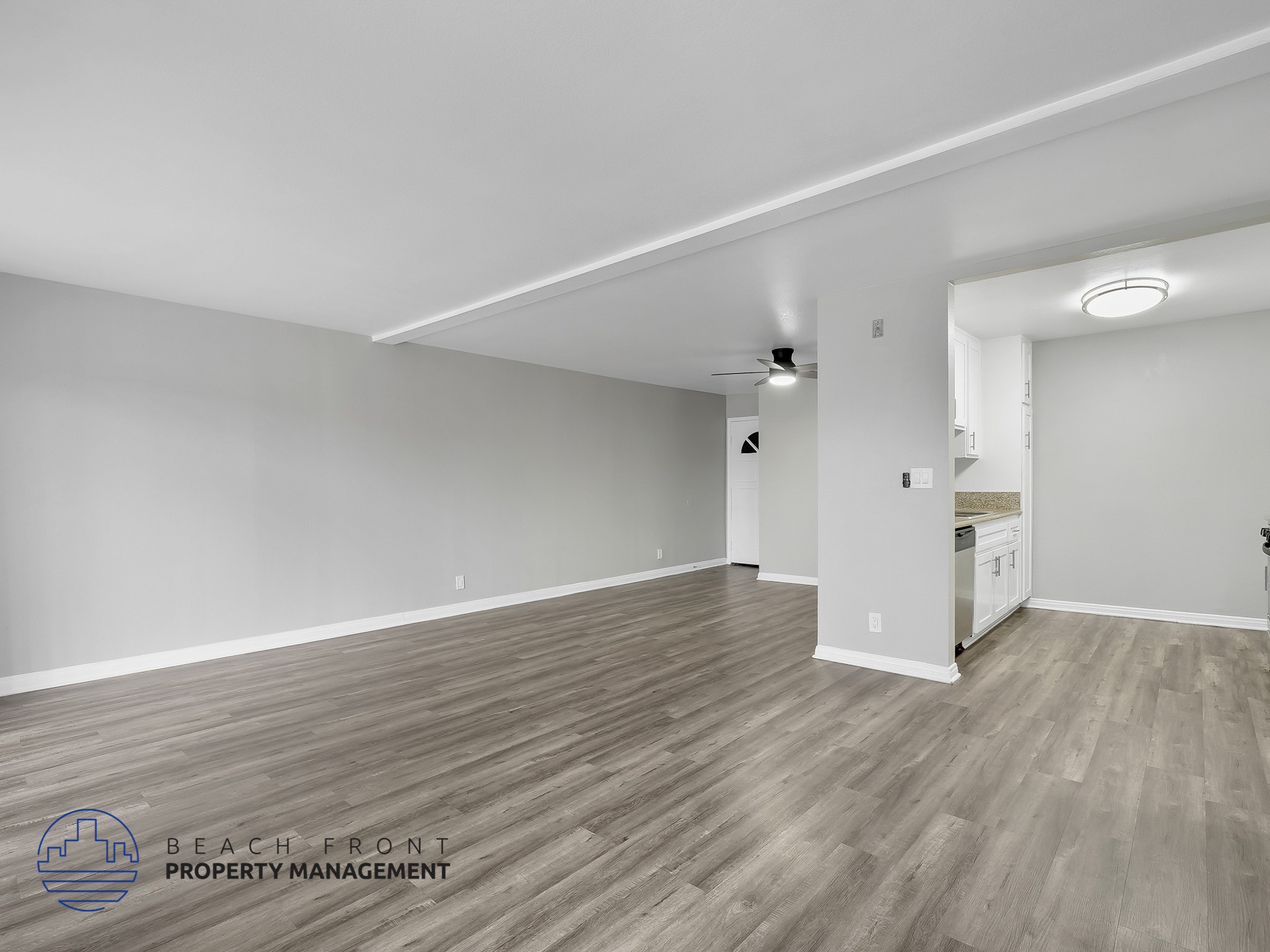 A spacious room with wooden flooring and white walls, with a logo for Beach Front Property Management in the bottom left corner.