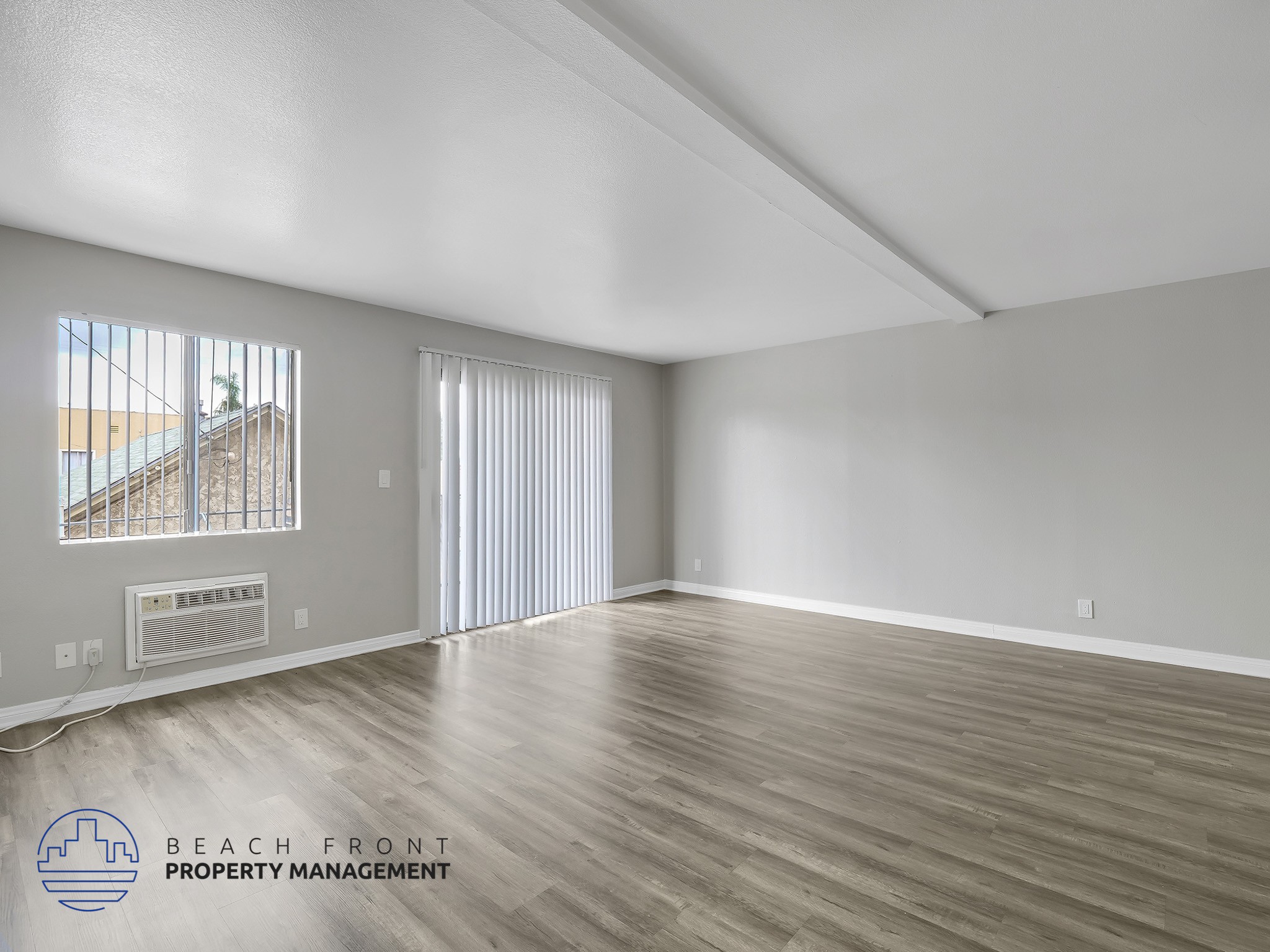 A spacious room with wooden flooring and a window overlooking a beach.