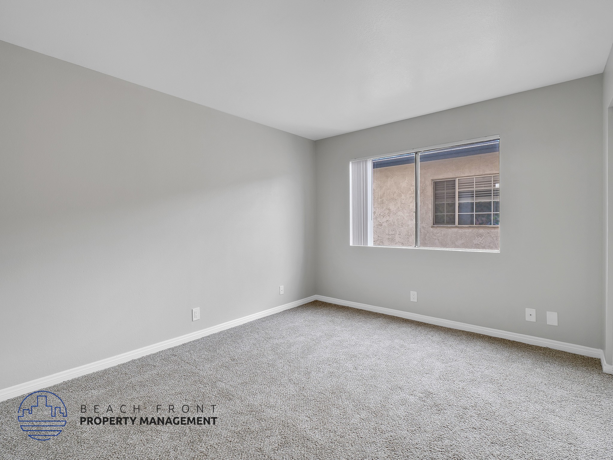 A spacious room with a carpeted floor and a window showing a building outside.