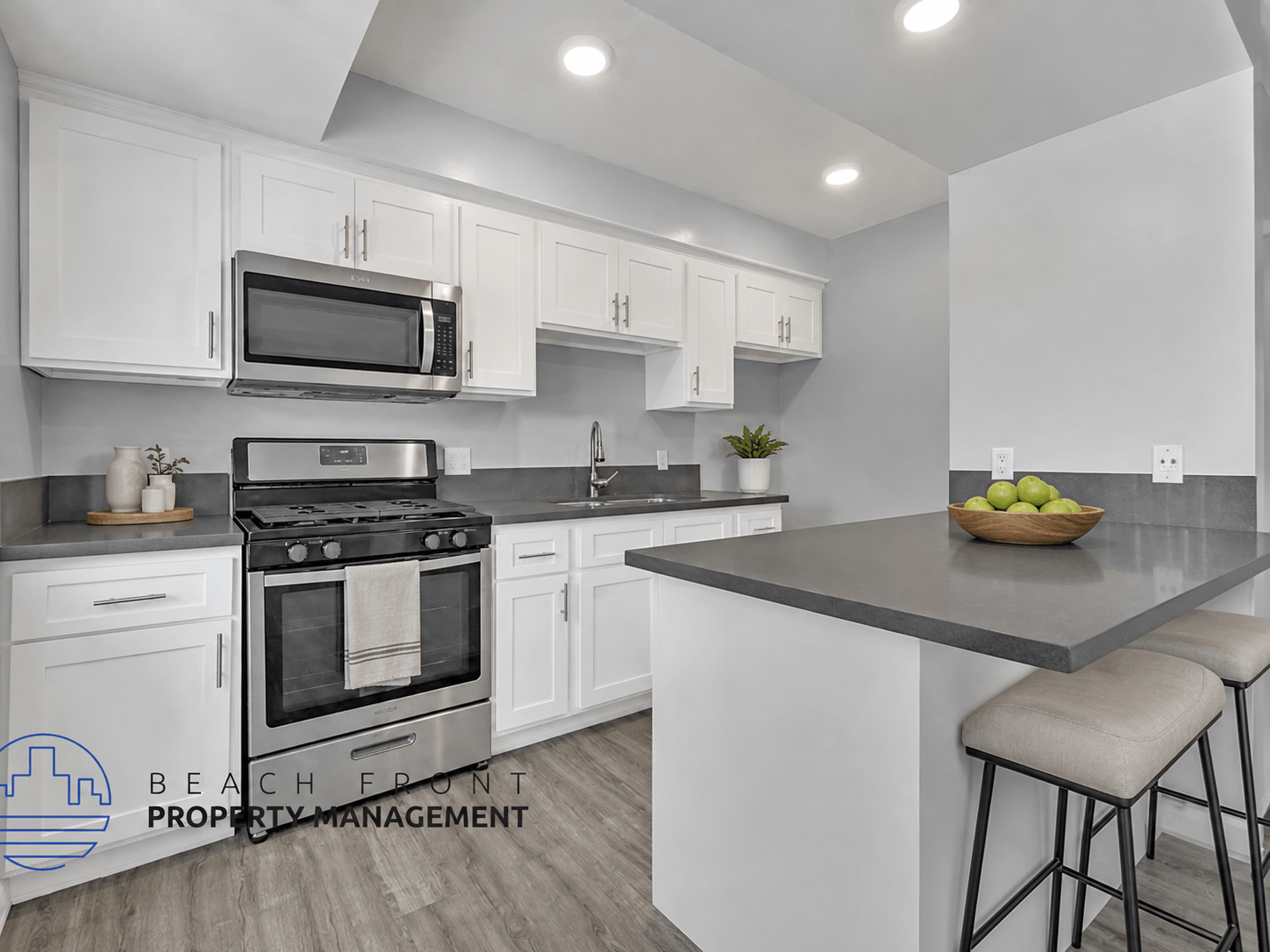 A modern kitchen with a stove, oven, microwave, and bar stools.