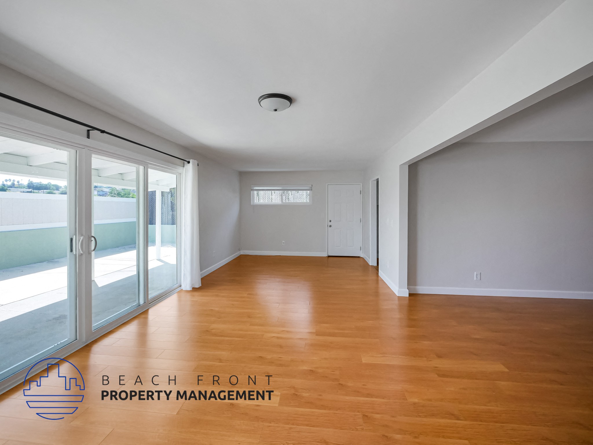 A spacious room with wooden flooring and a logo for Beach Front Property Management in the corner.