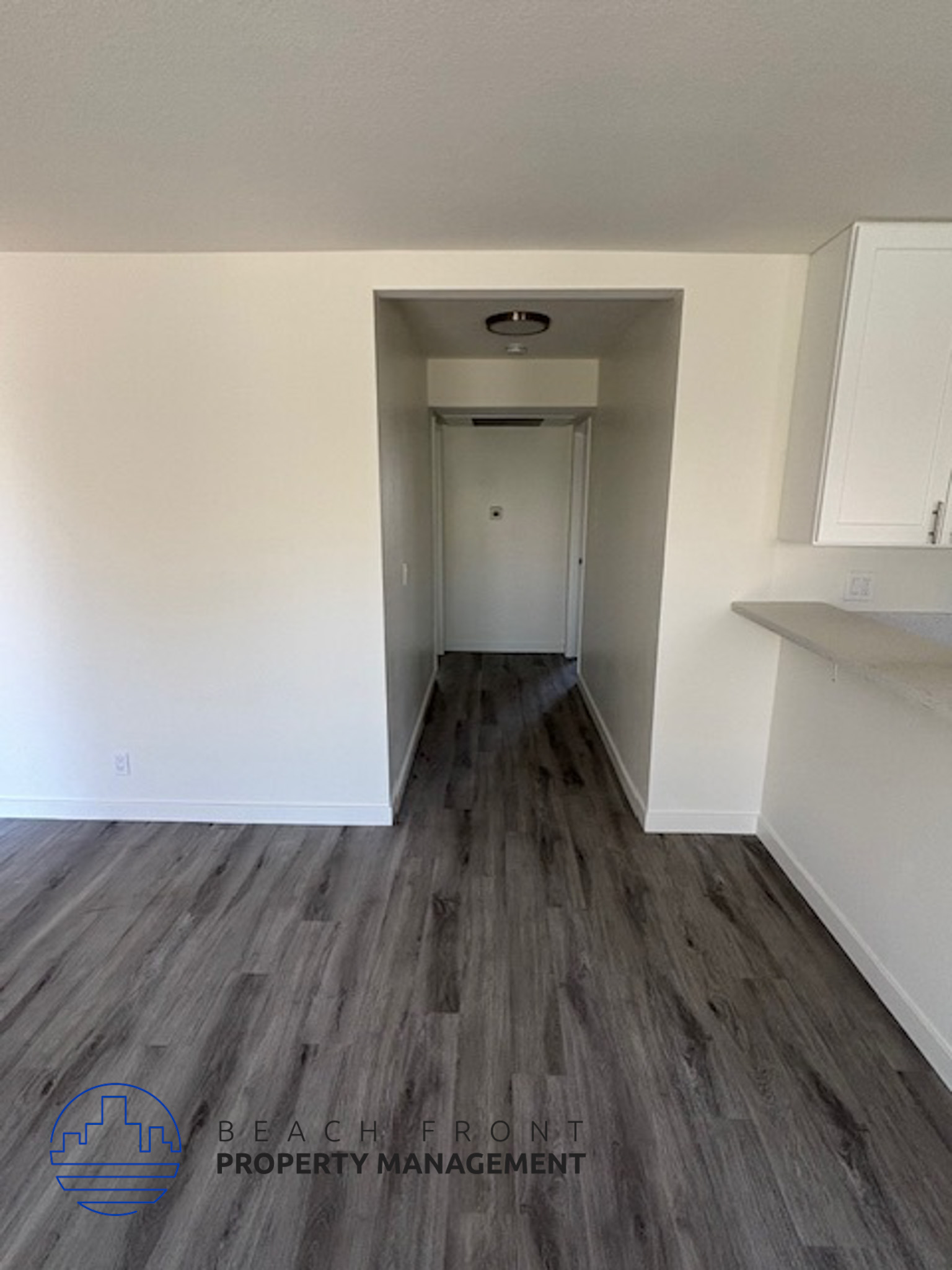 A hallway with wooden floors and white walls leading to a door.
