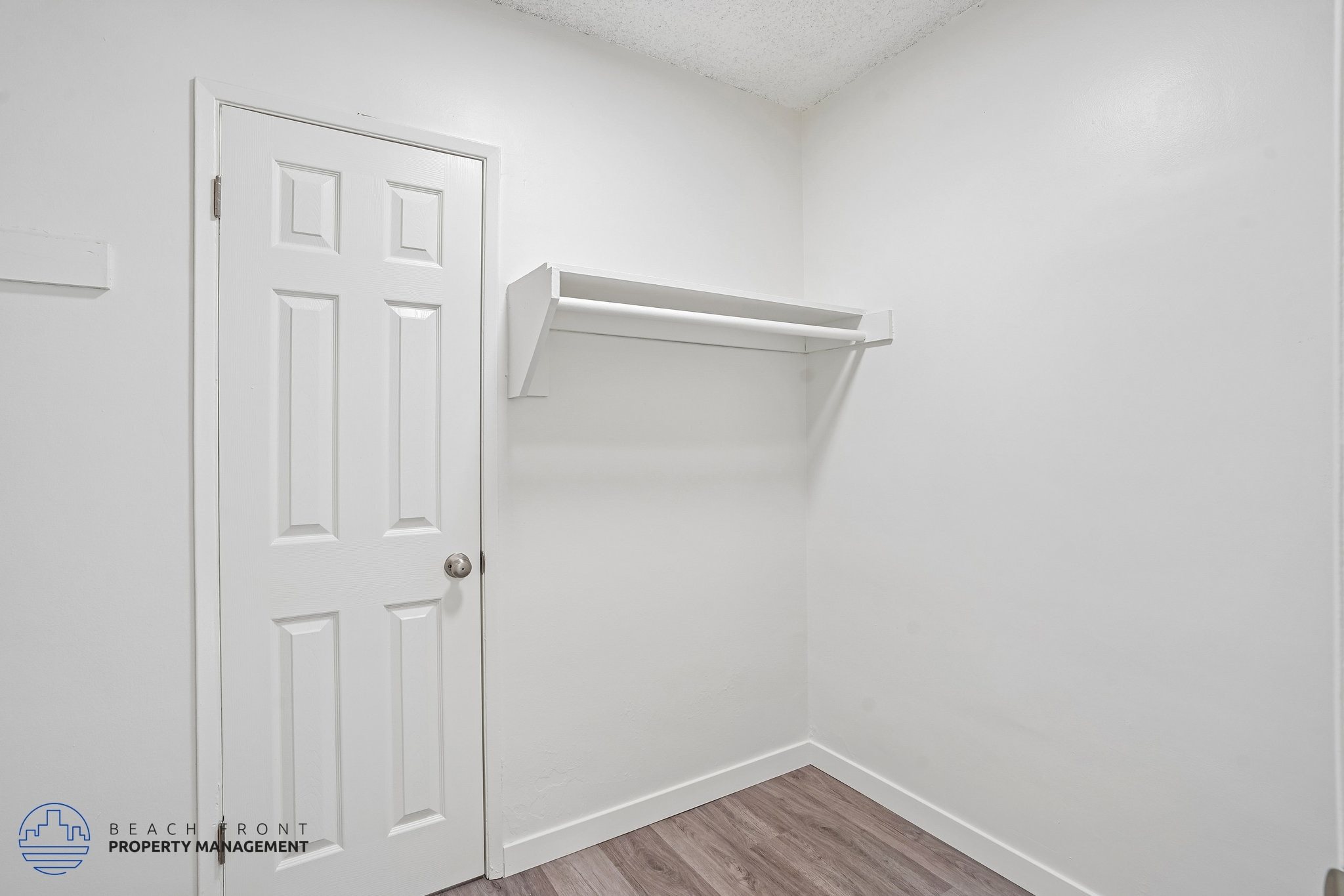 A white door is on the left of a white wall with a shelf on the right.
