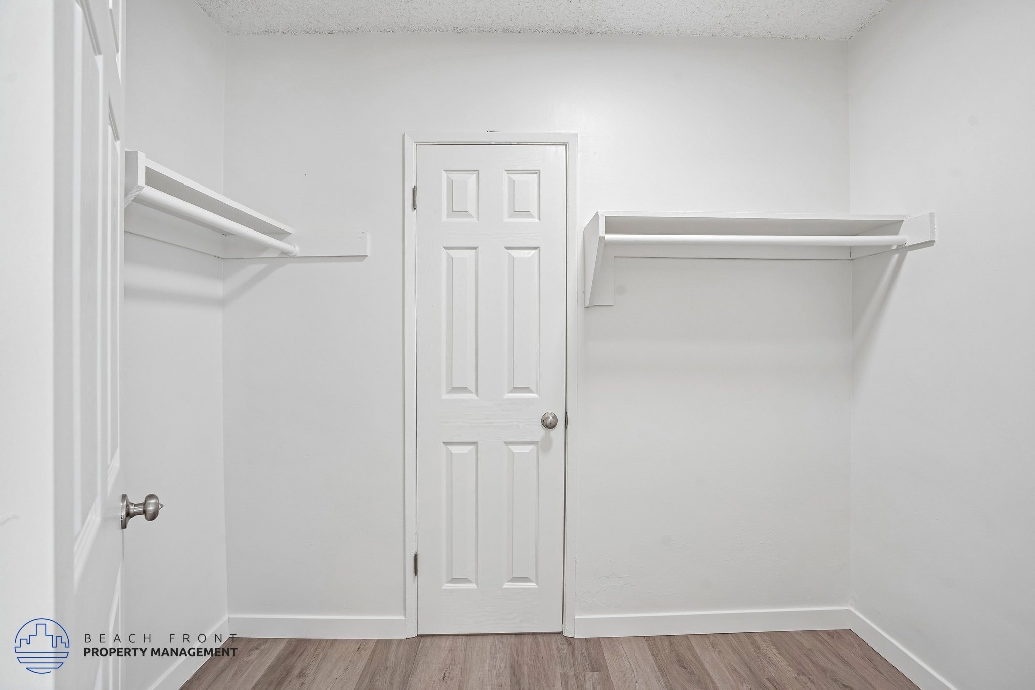 A white door is in the middle of a room with two shelves on the wall.