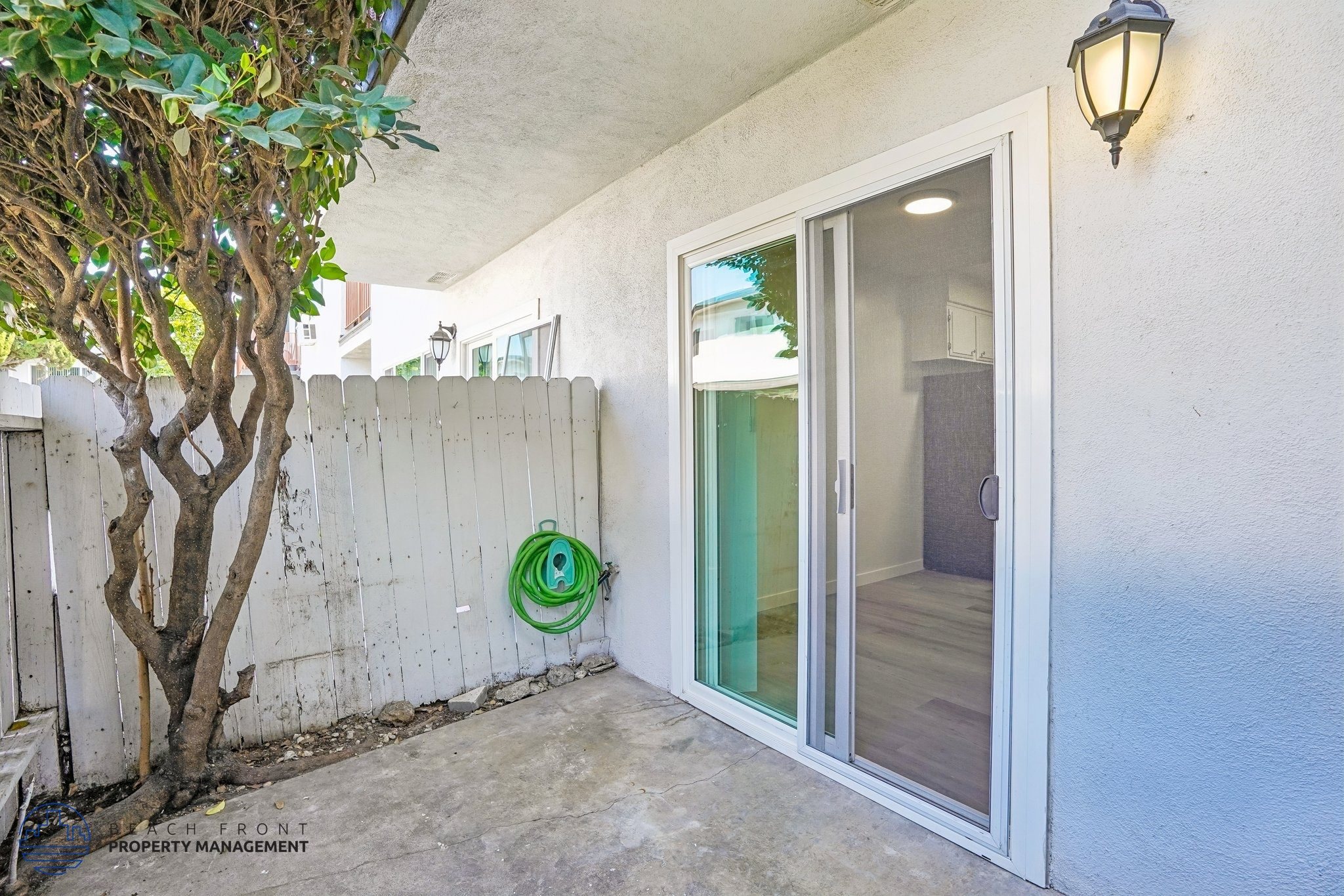 A patio area with a tree, a wall, and a sliding glass door.