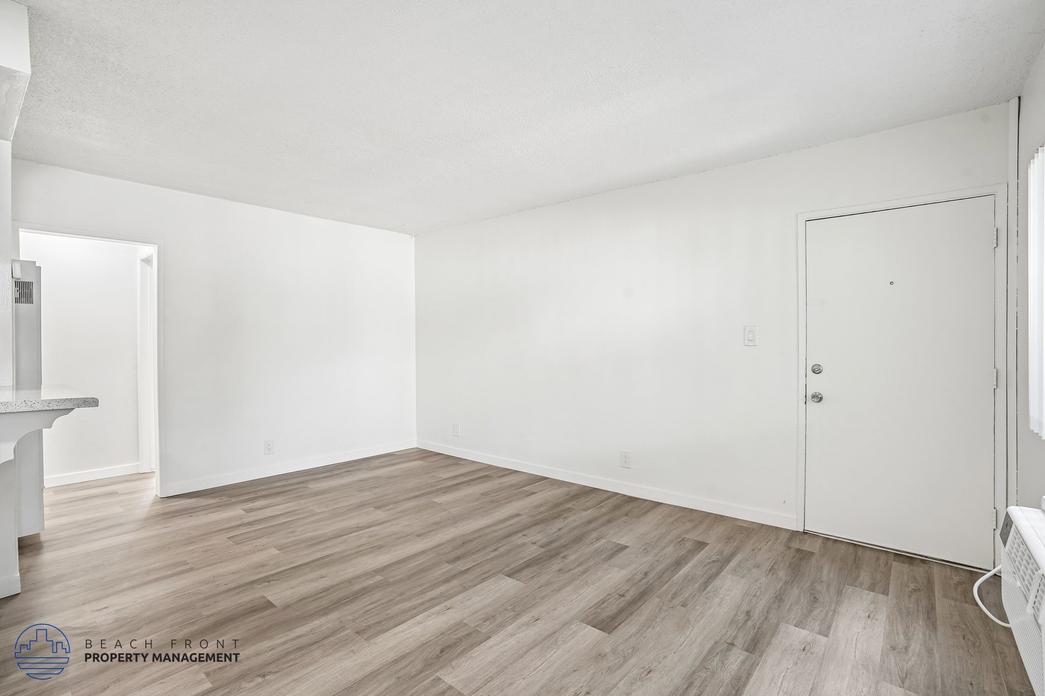 A room with wooden flooring and white walls, with a door on the right side.