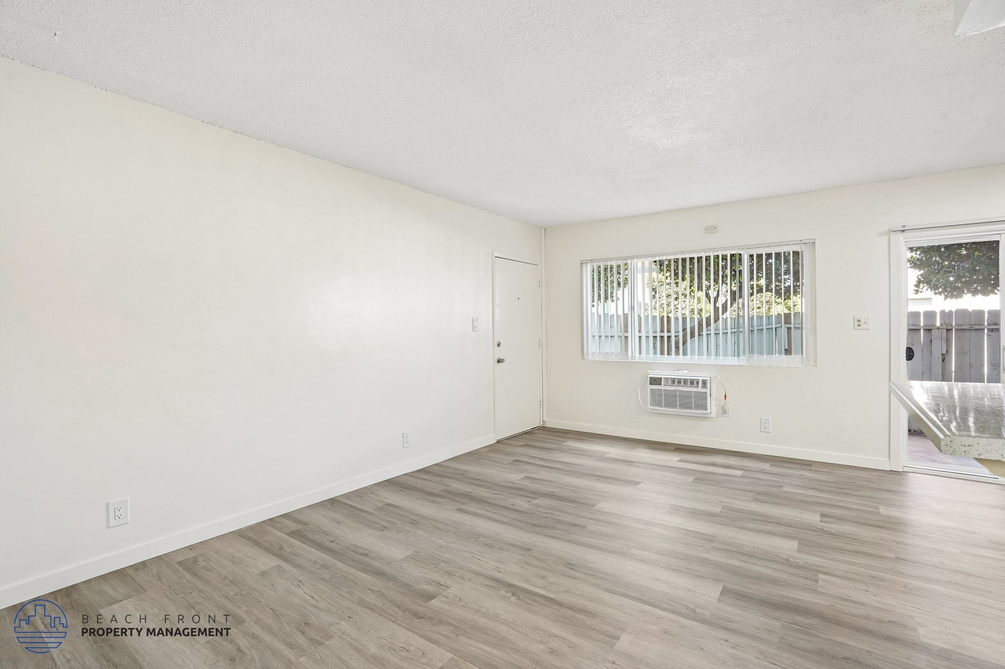 A spacious room with wooden flooring and a window with blinds.