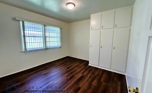 A room with wooden floors and white walls, with a window covered by a white blind.