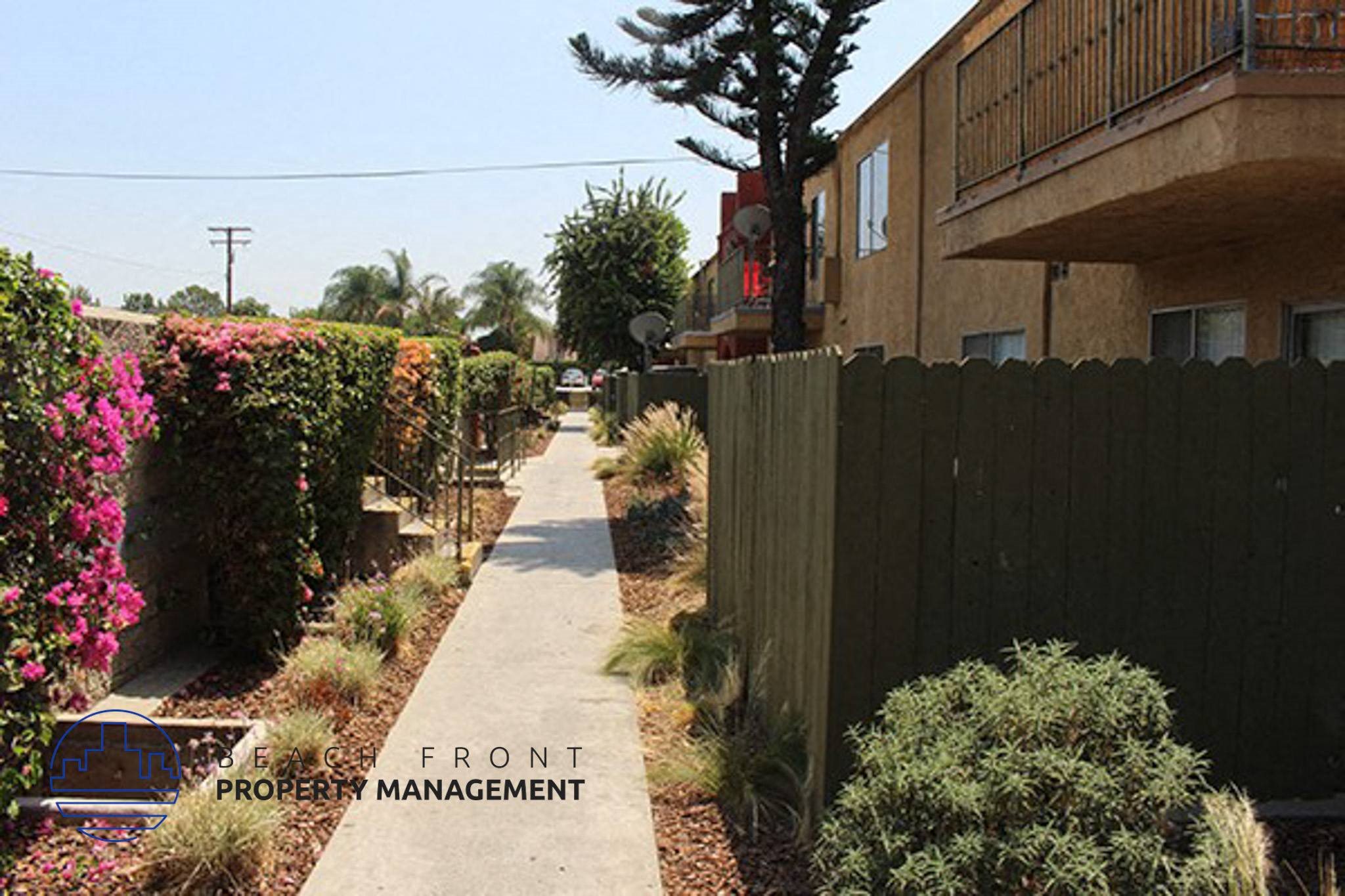 a sidewalk next to a fence and a building,a sidewalk next to a fence and a building