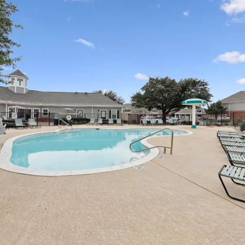 A large outdoor swimming pool with a diving board and a small building in the background.
