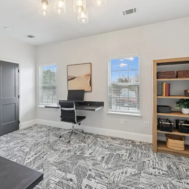A room with a black and white patterned carpet, a black chair, a wooden bookshelf, and a painting on the wall.