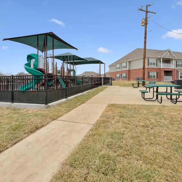 A playground with a green slide and a building in the background.