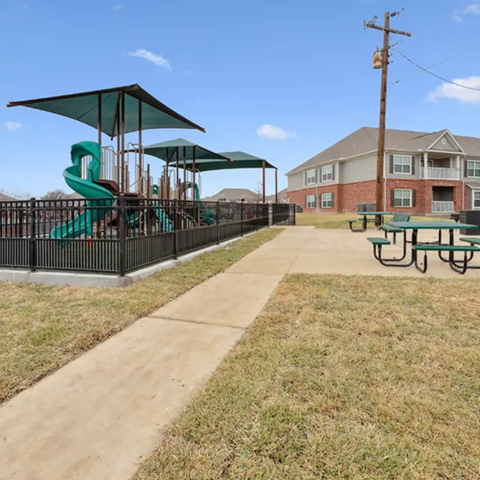 A playground with a green slide and a building in the background.