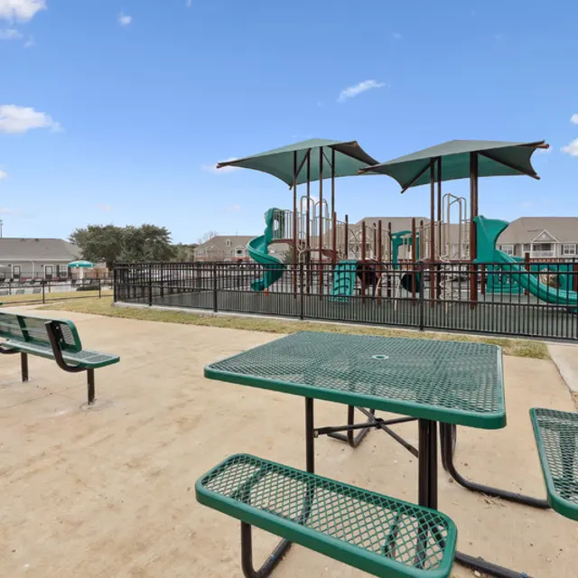 A playground with a green slide and a table with green chairs.