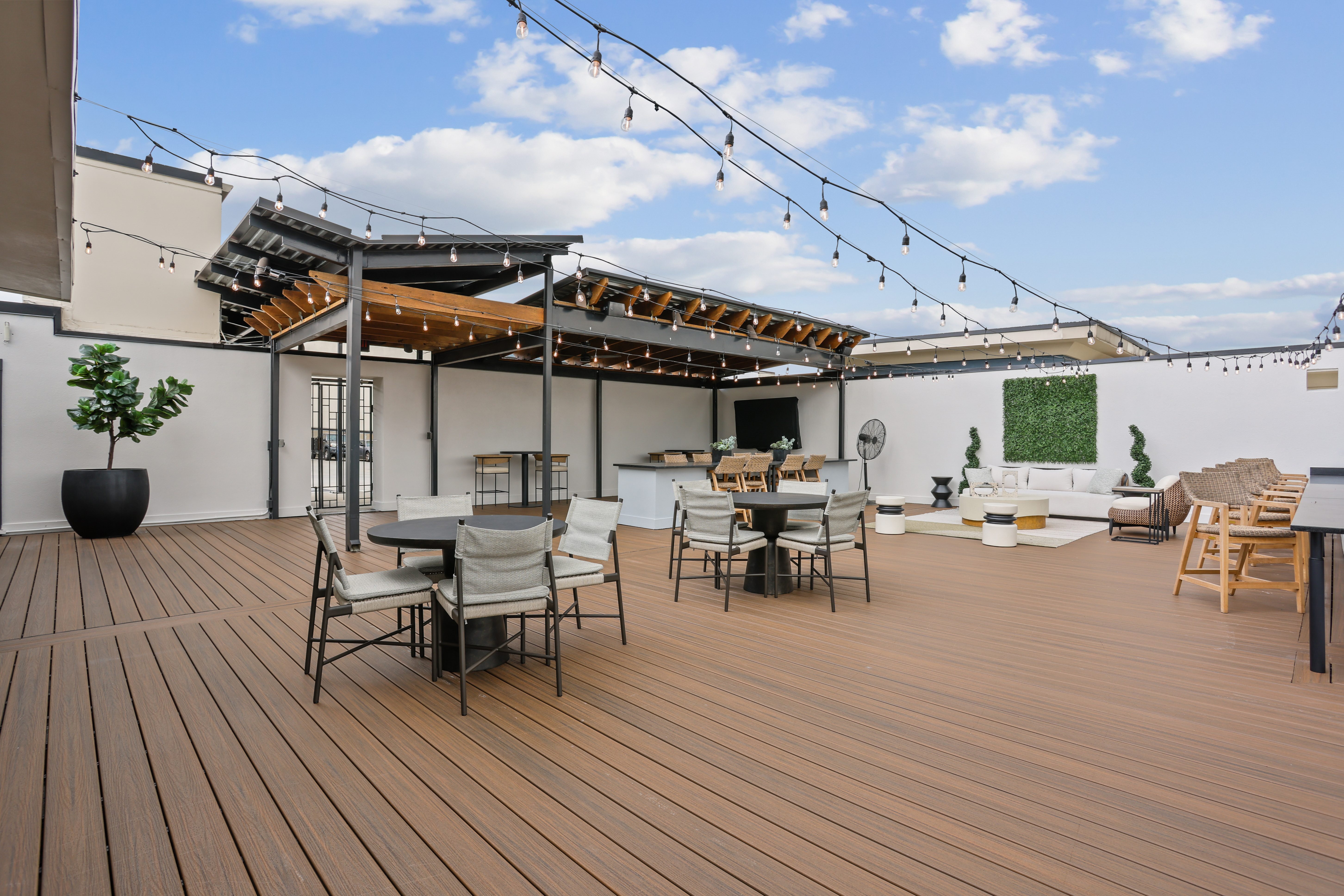 A wooden deck with chairs and tables is surrounded by a white building.