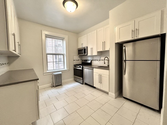 A kitchen with white cabinets and a stainless steel refrigerator.