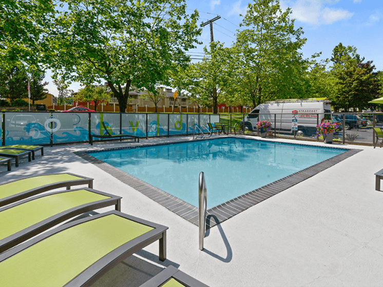 Pet-Friendly Apartments in Federal Way, WA - Colorful Fenced-In Community Pool Area with Lounge Seating and Shaded Areas