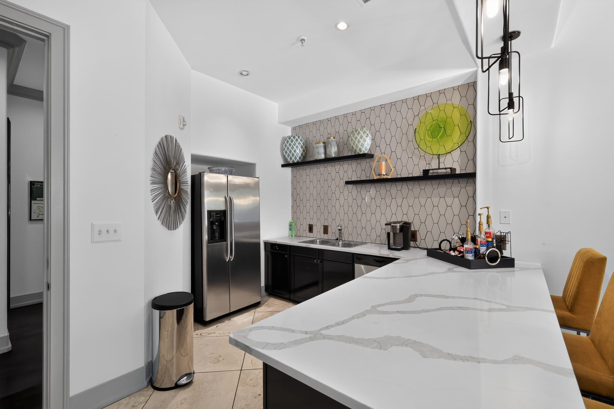 A modern kitchen with a marble countertop and a yellow chair.