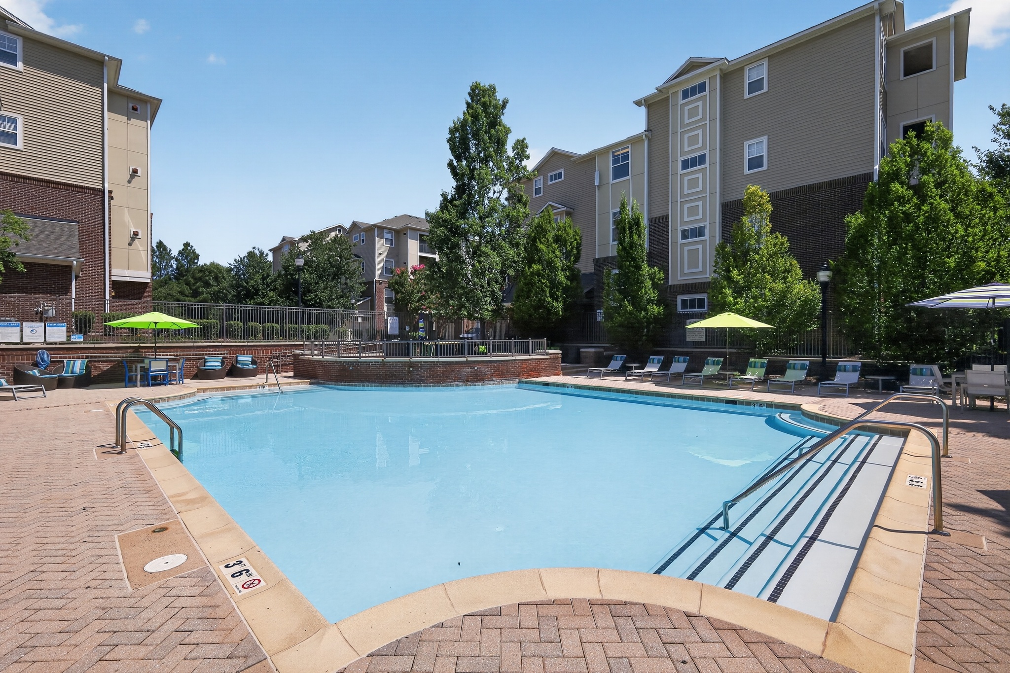 A large outdoor swimming pool surrounded by a brick patio and lounge chairs.