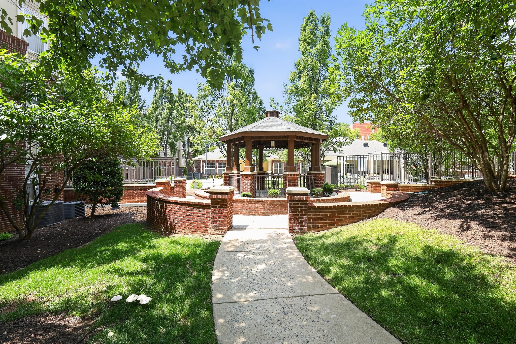 A gazebo is surrounded by a brick wall and a concrete walkway.