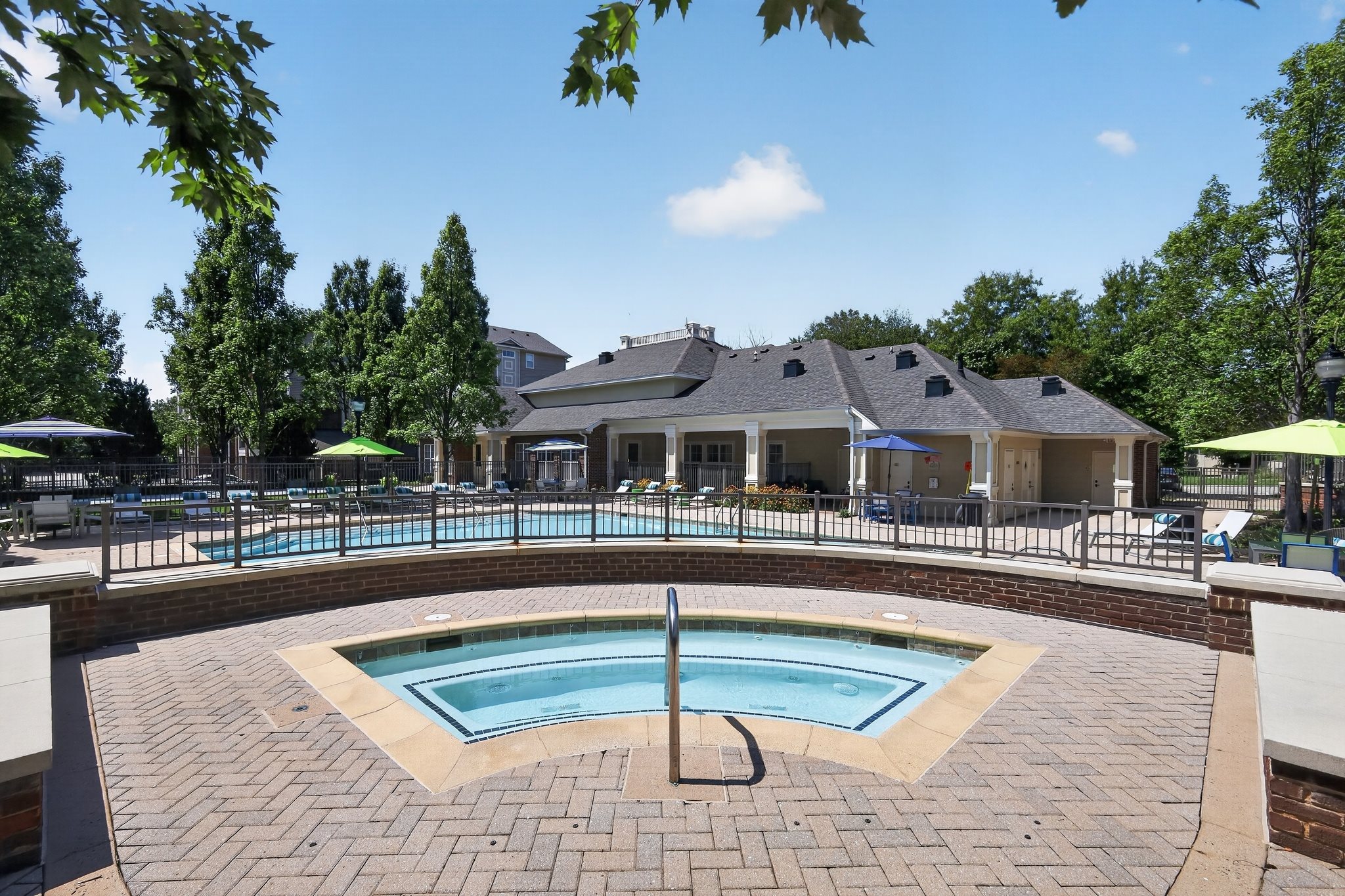 A pool surrounded by a brick patio with a house in the background.