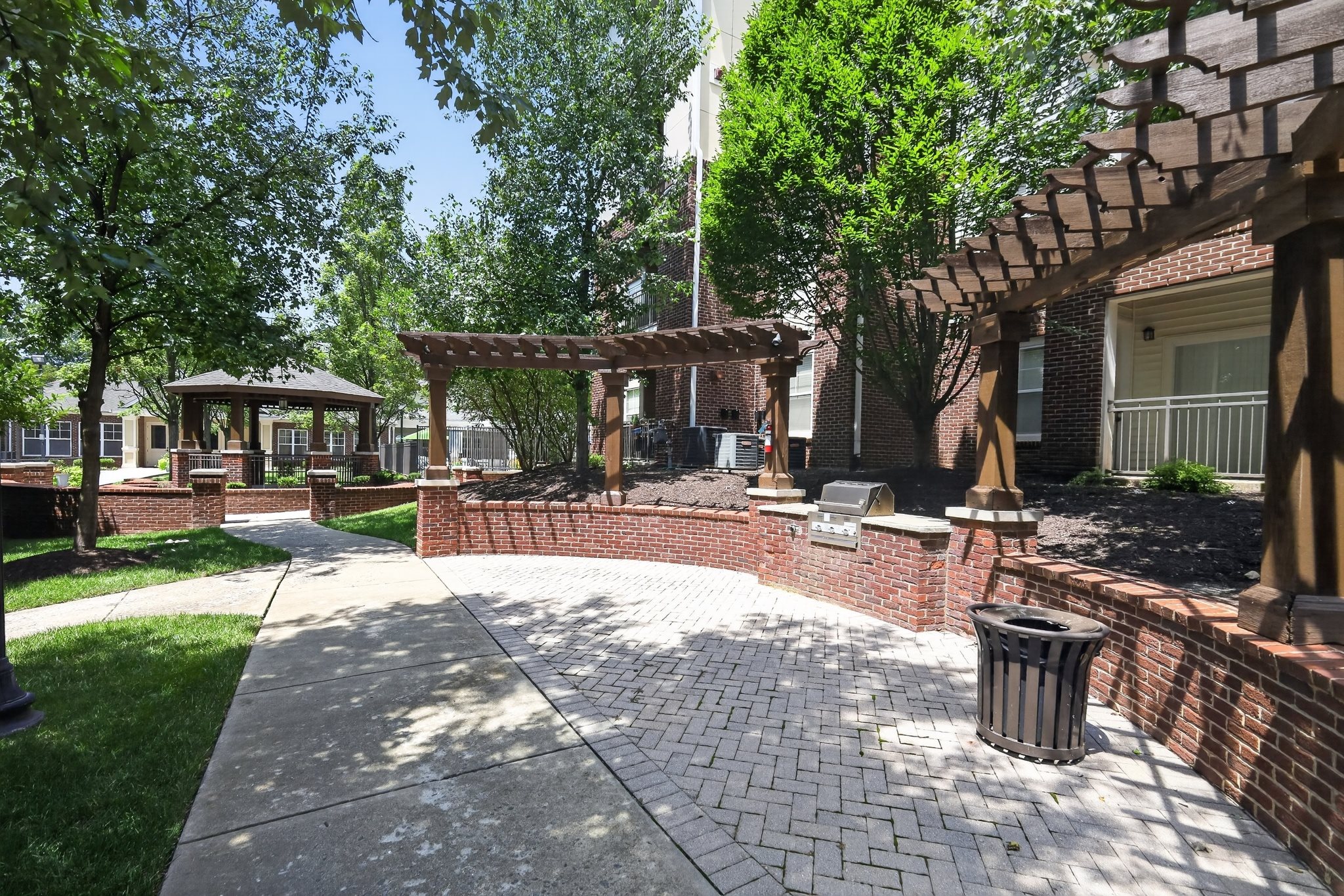A sunny day in a residential area with a brick wall and a trash can.
