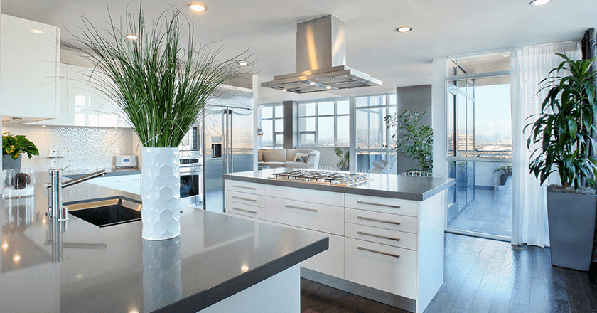 Pet-Friendly Apartments in Irvine, CA - Astoria at Central Park West - Bright Modern Kitchen With White Cabinets, Quartz Island, Stainless Range Hood, and Large Windows Opening To Balcony.