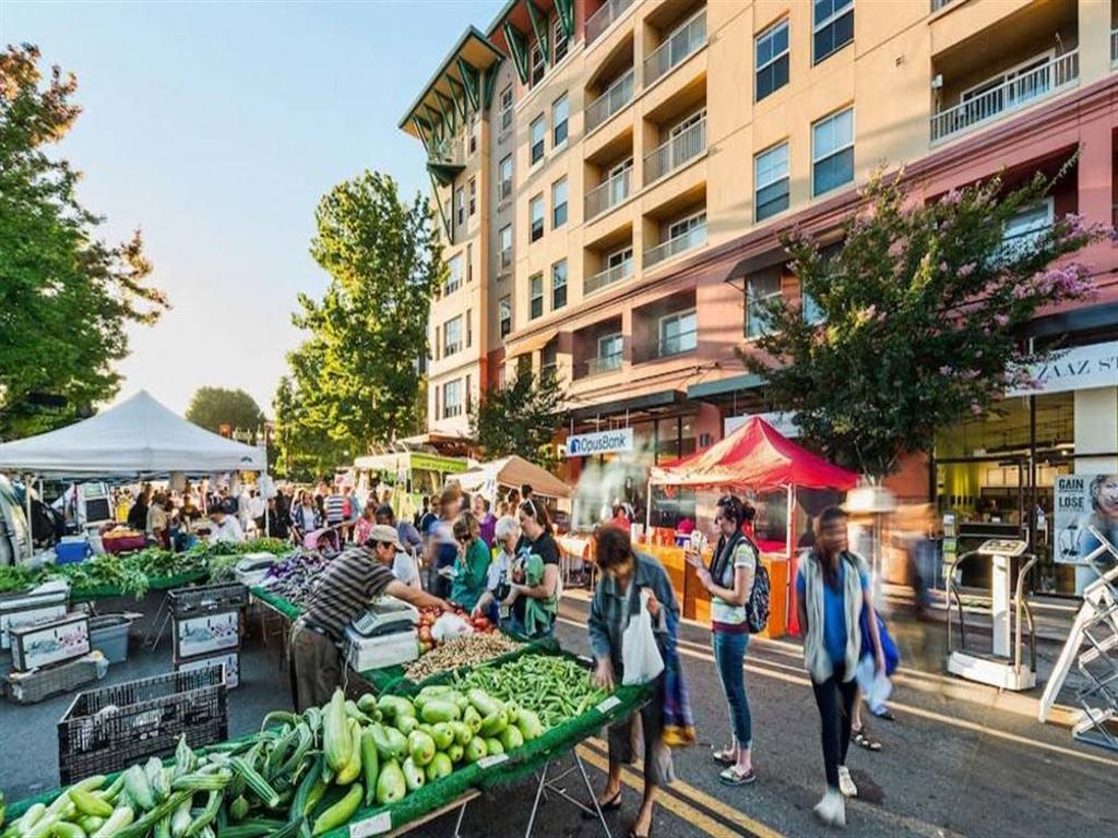 A busy outdoor market with people shopping and a building in the background.
