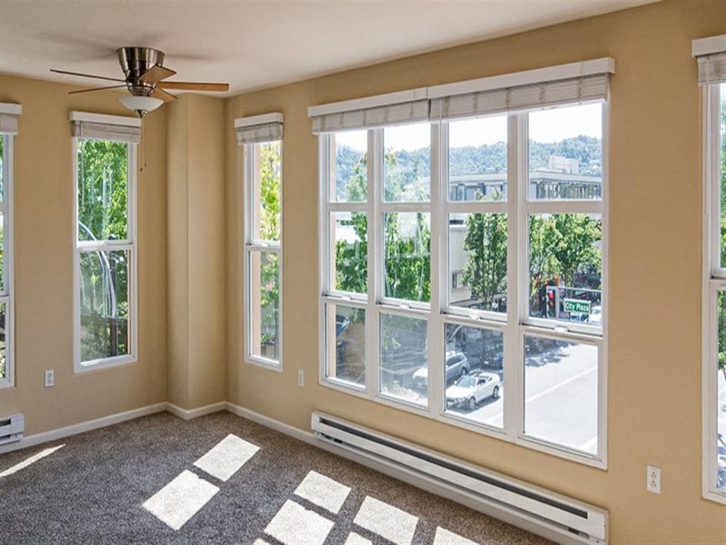 A room with a ceiling fan and large windows overlooking a street.