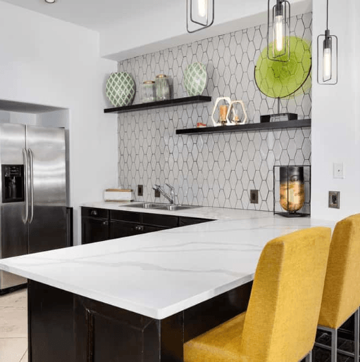 Modern kitchen with white quartz countertop, black cabinets, honeycomb tile backsplash, and yellow bar stools.
