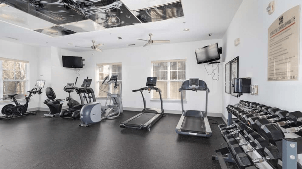 Apartment fitness center with treadmills, ellipticals, stationary bikes, and dumbbell rack.