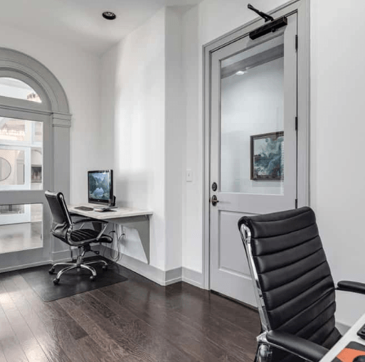 Modern office space with computer desk, rolling chair, and glass-paneled door.